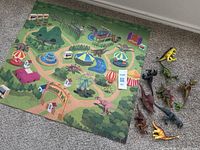 Felt play mat with dinosaur park illustration and 10 plastic dinosaur toys arranged beside it on the floor.