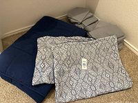 Photo of folded navy blue comforter and patterned shams with two sets of gray sheets folded and stacked