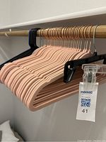 Velvety pink hangers, black plastic hangers and clear plastic pant hangers arranged on a rod.