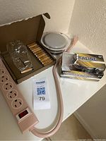 View of pink power strip, batteries, furniture gliders, and a small white round item on a white surface.