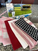 Dish towels laid out in various patterns in front of drying rack, gloves, sponges, and scrub brush on kitchen countertop