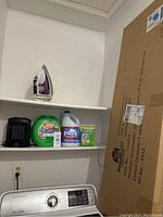 Iron, detergent pods, bleach, washing machine tablet, small space heater on shelves above Samsung washer
