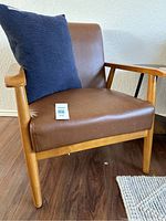 Brown faux leather accent chair with wooden frame, shown from angled front view with blue cushion on seat.