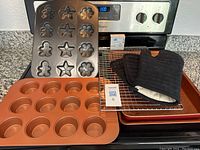 Full set shown with muffin tin, cookie/candy mold sheet on oven, baking sheet underneath, cooling rack, black oven mitt, and three pot holders grouped on the counter.