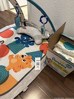 Infant play mat on floor with colorful cartoon animals and overhead arch, box containing Pampers Sensitive Baby Wipes beside it.
