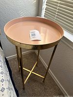 Front angled view of round rose salmon metal tray on gold metal frame and legs.