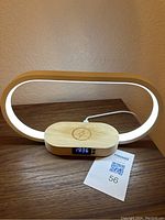 Oval-shaped LED side table light with glowing white light and wooden finish base featuring digital clock and wireless charging pad.