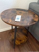 Full view of the round dark wood side table showing wood finish, legs, and lower shelf from an angled front perspective.