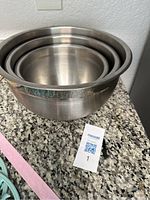Three nested stainless steel mixing bowls on granite counter, showing bowl interiors and rims.