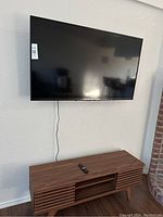 Front view of TCL 50-inch TV mounted on wall, showing black screen, black bezel, remote on media unit below.