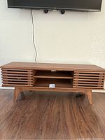 Front view of the walnut TV stand under a mounted flat panel TV, showing slatted doors and open shelves.