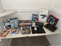 Photo showing all game and puzzle boxes arranged on a white shelf, including visual perception game, human anatomy puzzle, board games, and model kit.