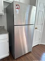 Full view of the stainless steel wide top-freezer refrigerator, closed, positioned beside white cabinets.