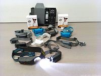 Full lot of 8 dog trainer collars and devices laid out on table including a box for Abbidot T30 E-Collar and collars of white, black, blue and grey colors with remote controls.