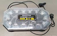 Top view of the clear rooftop strobe light showing LED bulbs and power cable with lighter plug.