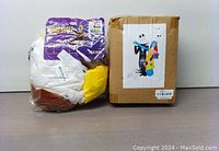 Photo of adult eagle costume inside clear plastic packaging showing brown, white, and yellow colors next to a sealed box.