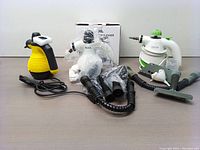 Three handheld steam cleaners displayed with accessories and cords on a flat surface, showing their colors and some attachments.