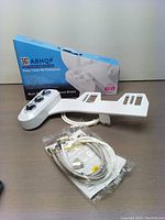 Photo showing ABHQP branded box, white plastic bidet attachment with control knobs, braided hoses, connectors, and manual laid out on table.