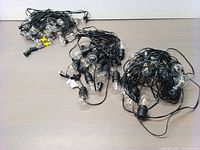 Photo showing three bundles of outdoor string lights with black cables and clear bulbs on a gray table.