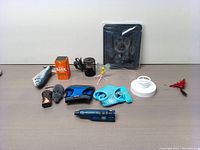 Photo showing all items in the pet toys and accessories lot arranged on a flat surface: pet screen door, anti-bark tool, spinning cat toy, two harnesses (large blue and small turquoise), remote control mouse, flopping fish toy, dog nail trimmer, and reptile heater lamp.