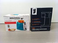 Photo showing boxed Holstein 2-slice toaster and black mini single serve coffee maker box side by side.