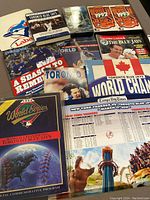 Overview of all included items laid out on a surface, featuring books, magazines, VHS tapes, commemorative programs, and posters related to Toronto Blue Jays World Series championships.