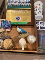 Photo showing Blue Jays plaque, trading cards, Blue Jay figure, a couple of baseballs inside a glass, and a small jigger cup.