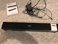 Speaker, remote, power cable, and owner's guide arranged on carpet