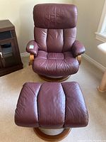 Front perspective of burgundy leather swivel recliner chair with ottoman in foreground