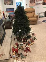 Artificial Christmas tree standing assembled with multiple small Christmas decorations spread in front along the fireplace.