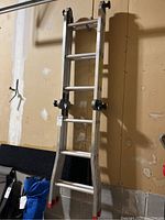 Full view of Featherlite aluminum combination ladder hanging against garage wall showing red rubber feet and locking mechanisms.