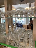 Wide view of various sizes of crystal stemware and other items on mirrored shelf.