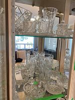 Wide view of crystal and glassware on a display shelf showing multiple vases, bowls, and small decorative items.
