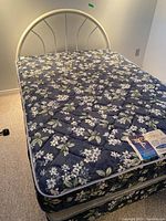 Full bed setup with floral mattress and matching boxspring on metal frame with off-white metal headboard.