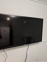 Front view of 32 inch Hisense flatscreen TV mounted on wall, black bezel with cables hanging down.