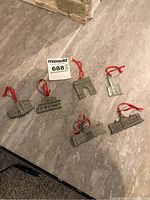Photo of six pewter ornaments depicting various Kingston landmarks laid out on stone surface, with red hanging ribbons visible