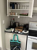 Kitchen cabinet and countertop with thermoses, mugs, glass jars, electric kettle, utensils, and boxed items visible