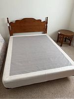 Full view of queen size bed with headboard and boxspring in bedroom corner near round side table.