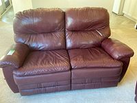 Front view of brown leather-like recliner loveseat showing cushioned armrests, backrests, and seat cushions with visible wear and creasing.