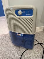 Full front view of the Simplicity 20 dehumidifier showing the off-white slatted front and translucent blue water tank.