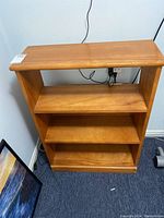 View of front and side of small wooden bookcase with three shelves and rounded top edge.