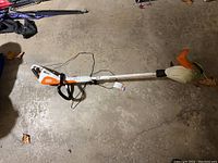 Full side view of Stihl FSA 45 weed trimmer showing long shaft and orange trimming guard lying on concrete floor.
