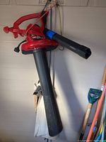 Front view of Toro Ultra Blower Vac hanging, showing the red body, black blower tube and attached fabric vacuum collection bag below. Loose blower attachment is visible.