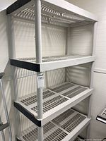 Front angle showing full height and five shelves of white plastic utility shelving with black corner reinforcements.