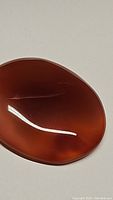 Close-up image of a deep orange carnelian oval cabochon gemstone showing its smooth polished surface and translucent nature.