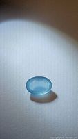 Close-up photo of the oval cut aquamarine gemstone showing vibrant sky blue coloration and smooth polish.