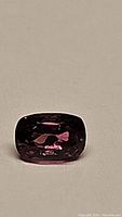 Close-up of natural intense pink spinel gemstone showing cushion cut and color under direct light.