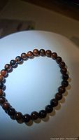 Top view of a round bead bracelet with alternating brown and black tones on a stretchy band, under bright light.
