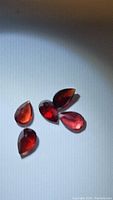 Five pear-shaped cherry red Mozambique garnet gemstones viewed with light reflecting off facets.