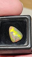 Pear-shaped Ethiopian opal held between fingers, showing bright multicolor play-of-color against black background in a display box.